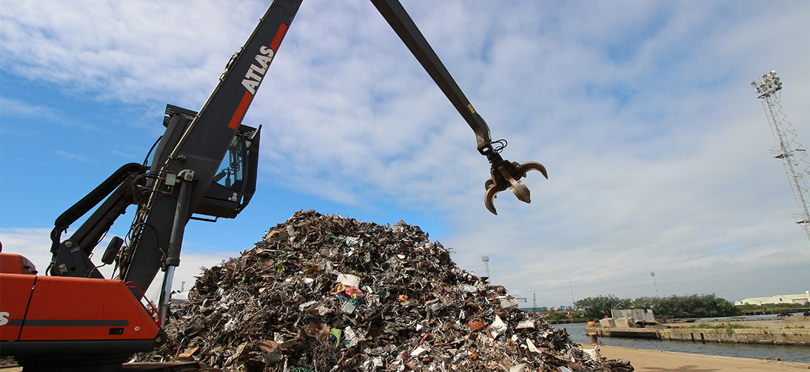 Photo of an articulated grabbing arm hanging over a pile of scrap metal.
